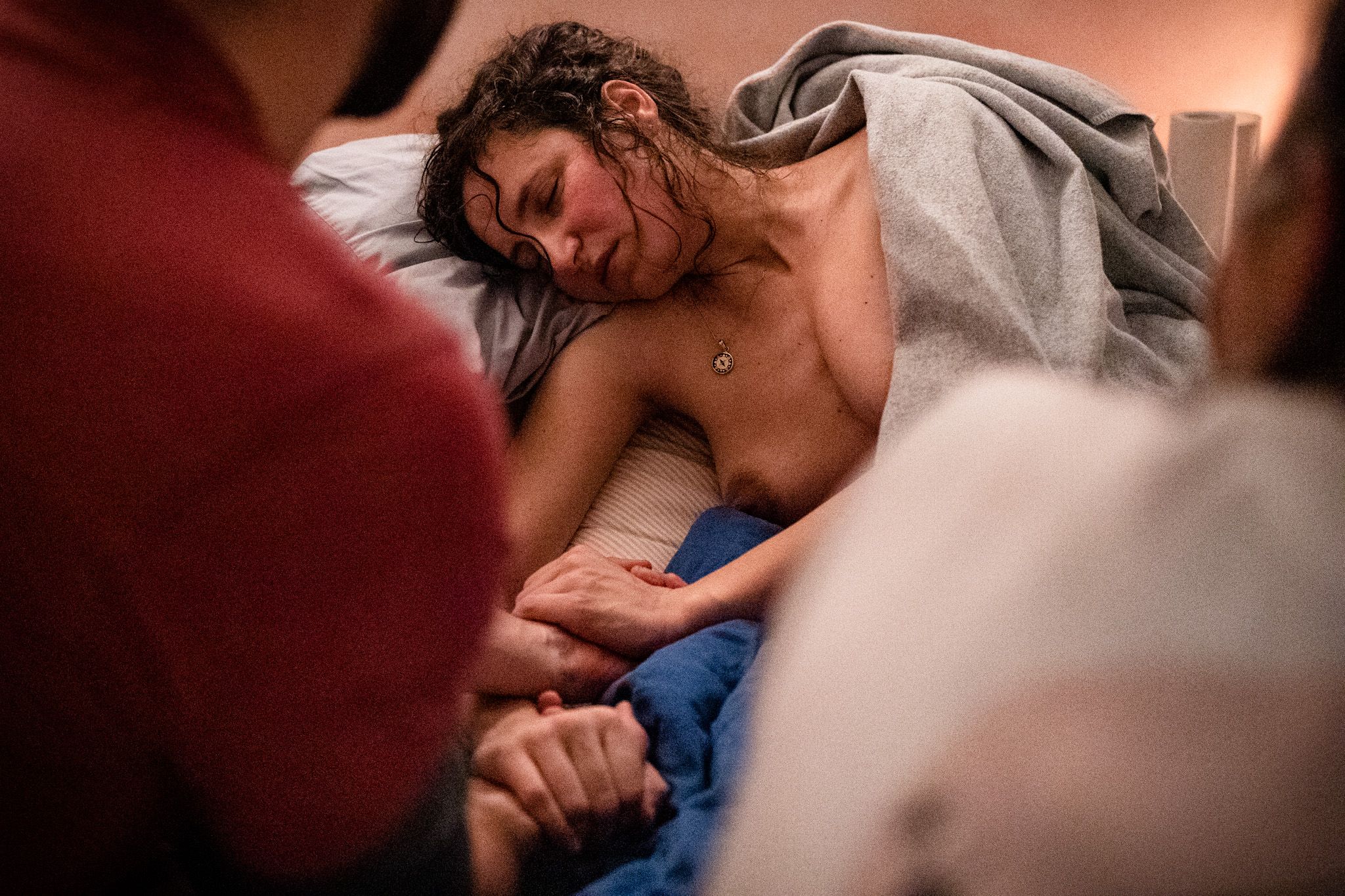 Eine Frau bei der geburt. Sie liegt erschöpft mit geschlossenen Augen da. Ihre Hände werden von ihrem Partner gehalten.