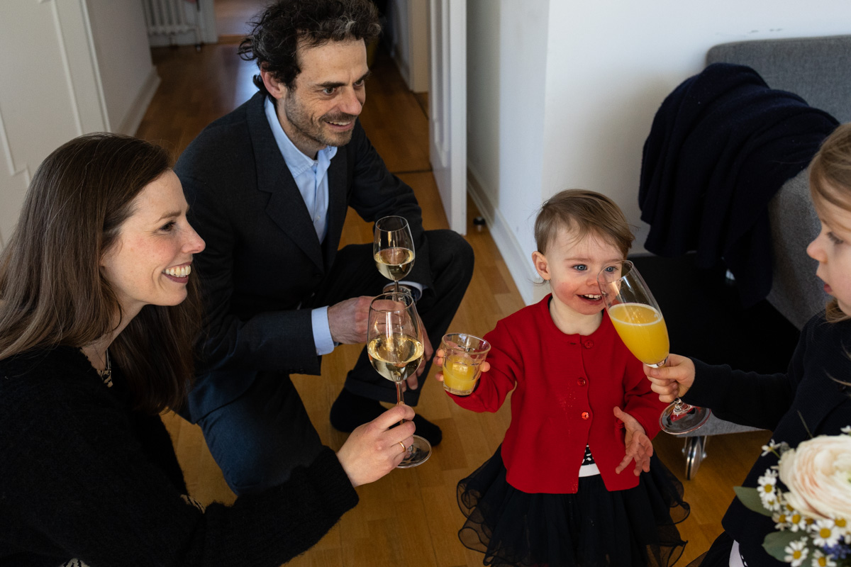 Eine Familie beim Anstoßen während einer kleinen Feierlichkeit. Zwei kleine Mädchen stoßen mit Orangensaft an, die Eltern mit Champagner.
