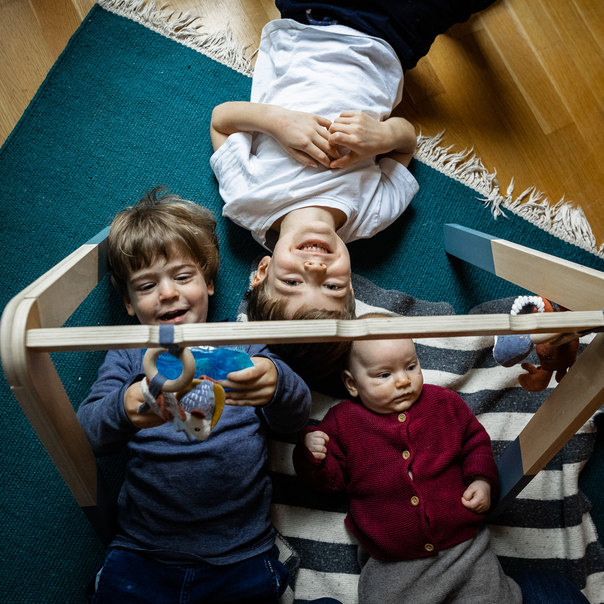 Drei Kinder liegen unter einem Spielbogen: zwei Jungen und ein Baby.