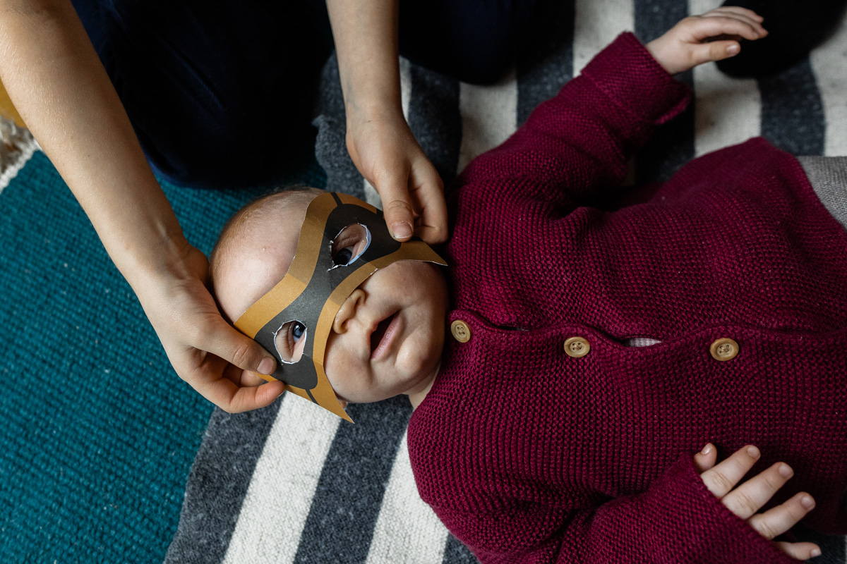 Einem Baby wird eine Superheldenmaske vors Gesicht gehalten.