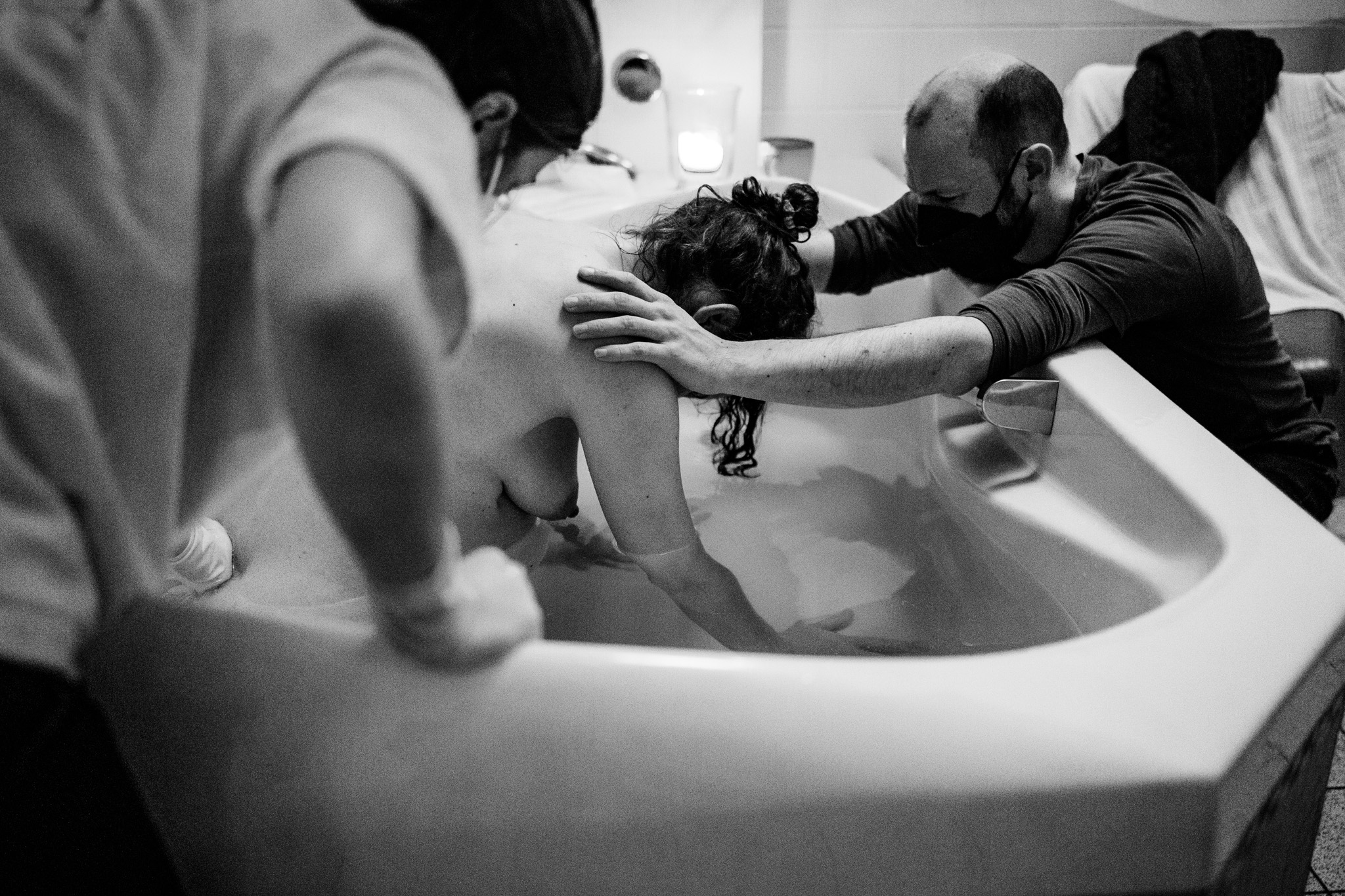 Geburtsreportage. Frau bei einer Wassergeburt. Eine Hebamme massiert ihren Rücken, der Mann hält sie an den Schultern.