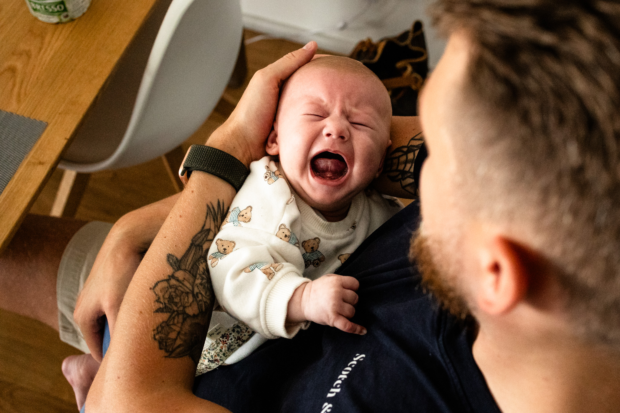 Wochenbettreportage, Geburttsfotografie: Ein weinendes Baby auf dem Arm seines Vaters