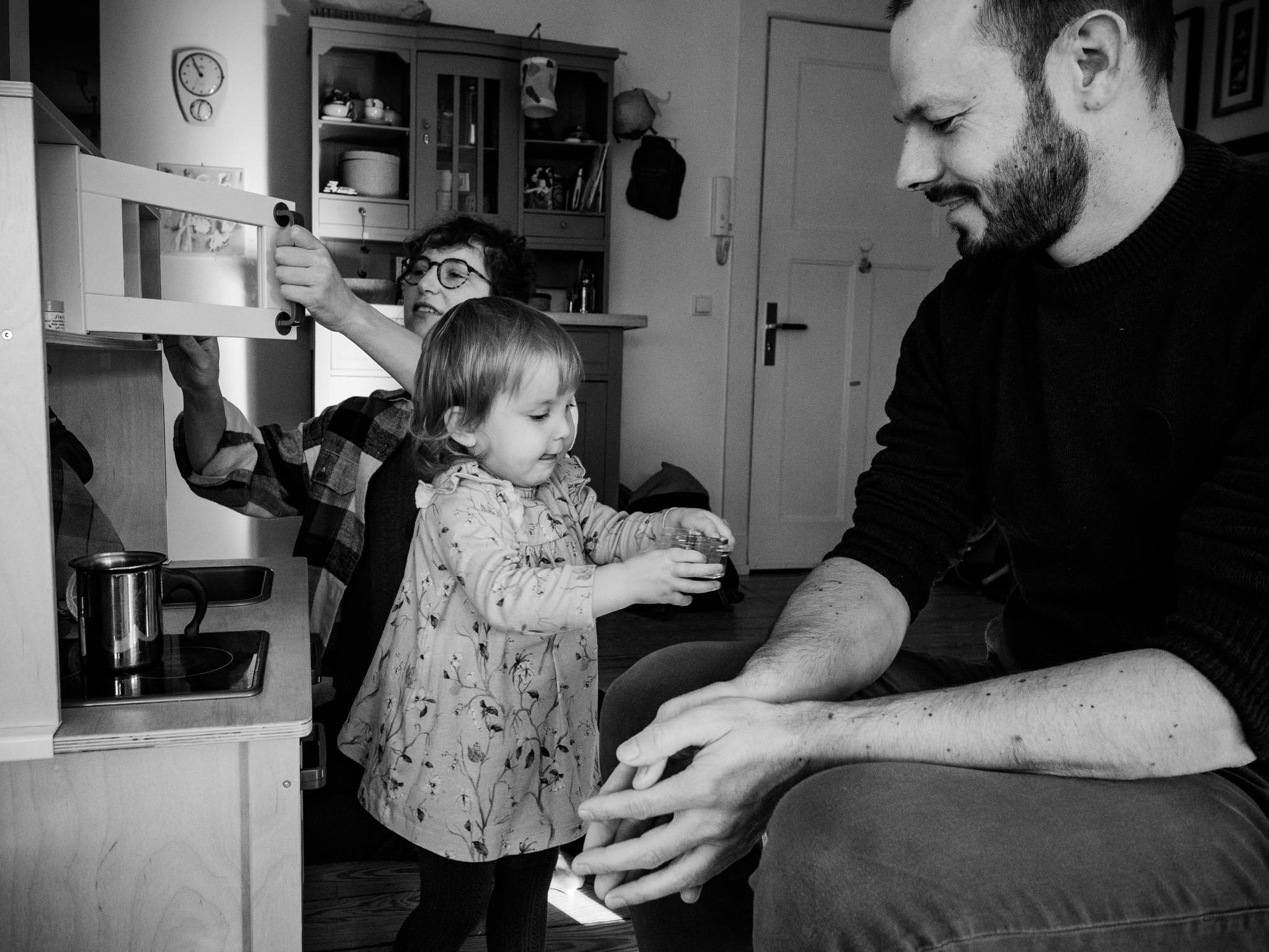 Familienreportage: Vater, Mutter und ein kleines Mädchen spielen in einer Spielküche zuhause
